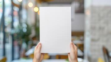 Blank White Paper Held by Hands in Restaurant Interior with Blurred Lights and Plants for Menu Design, Advertising, or Presentation Mockup, Daylight Setting, Vertical Orientation photo