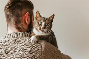 Cat Day concept. Warm Embrace With Cat, Brown Tabby Cat On Man's Shoulder, Cozy Knit Sweater, Soft Light, Home Interior, Relaxed Atmosphere, Candid Moment, Comfortable and Quiet, Feline Bonding. photo