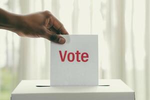 Hand Placing Vote Card in Ballot Box with Vote Text in Election Concept, Democracy Process, Political Participation, Government Voting, Civic Duty Image, Close-Up photo