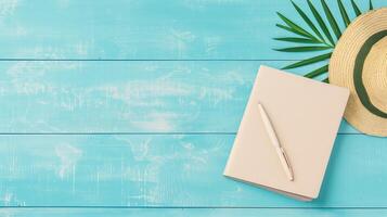 Top View of Notebook, Pen, and Straw Hat on Blue Wooden Copy Space Background with Palm Leaf - Summer Travel, Study, or Creative Writing Concept photo
