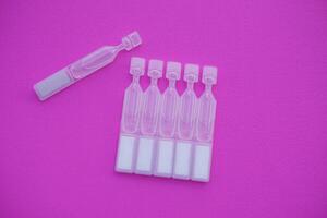 Single use artificial tear lubricant eye drops containers, tubes, isolated on pink background. Concept, medical products for dry eyes or eyes disease treatment. photo
