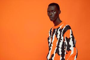Trendy male model in a stateMalet sweater with graphic print and a bright orange background highlighting a high fashion portrait and a vibrant lifestyle photo