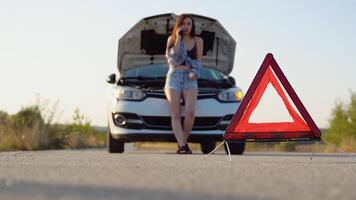 Road side warning triangle, warning oncoming traffic of a broken down car, with a woman using her cell phone to call for assistance video