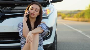 Upset young woman driver talking angrily on phone with assistance service near a broken car with open hood while inspecting engine having trouble with her vehicle video