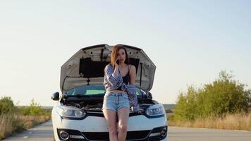 Upset young woman driver talking angrily on phone with assistance service near a broken car with open hood while inspecting engine having trouble with her vehicle video
