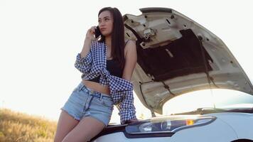 Upset young woman driver talking angrily on phone with assistance service near a broken car with open hood while inspecting engine having trouble with her vehicle video