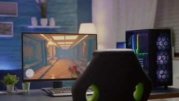 RGB powerful personal computer gamer rig with first-person shooter game on screen. Monitor stands on table in home gaming room. Cozy room with modern design is lit with warm and neon light. video