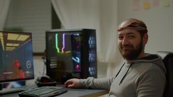 Portrait of happy man looking at camera smiling playing online FPS shooter videogame for virtual tournament. Cyber performing on powerful computer with RGB keyword during championship at home video