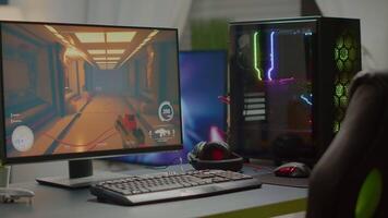 RGB powerful personal computer with first-person shooter game on screen in gaming studio with no people at desk. Empty cozy room with modern design is lit with warm and neon light. video