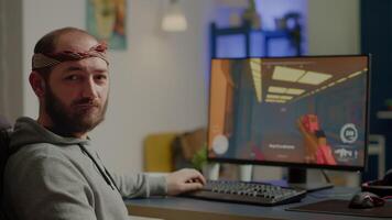 Pro cyber man looking at camera before playing space shooter videogames using professional RGB keypad on powerful computer. Professional player performing during online gaming championship late night video