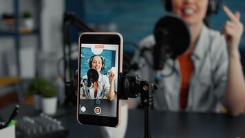 Smartphone device recording creative digital content creator telling life stories. Vlogger filmed with touchscreen cellphone while talking to audience sitting at home studio desk. Close up video