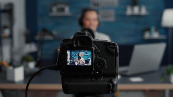 Professional modern camera recording internet star talking to audience. Popular social media content creator filming vlog for sharing platforms while sitting at studio desk. Close up video