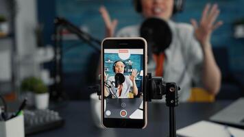 Modern smartphone recording vlogger talking to public while sitting at home studio desk. Famous influencer filming podcast show with touchscreen display device while sitting in living room. Close up video