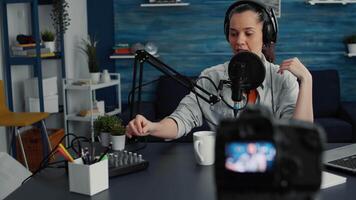 Attractive social media influencer speaking to audience at microphone while tweaking sound using professional mixer. Creative digital content creator recording podcast at home studio. video