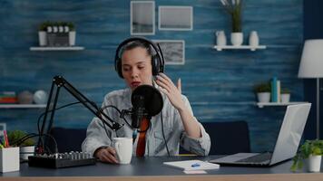 Attractive digital content creator checking microphone while recording daily vlog. talk show host speaking to audience about last world events and news while sitting at home studio desk. video