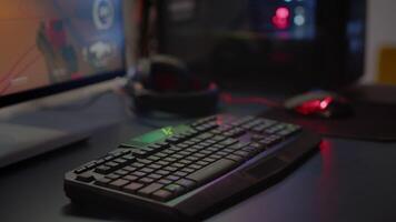 Close up of professional RGB keypad in empty gaming room prepared for streaming online tournament, display with first person shooter playing on it. Game studio with powerful computer video