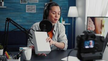 Creative tech enthusiast recording unboxing with professional camera while presenting device specifications to audience. Digital content creator unpacking promoted product while doing review. video