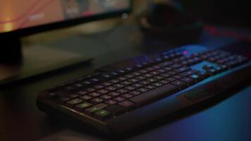 Close up of professional keyboard with RGB lighting prepared for streaming online tournament, display with first person shooter playing on it. Gaming studio of esport game with powerful computer video