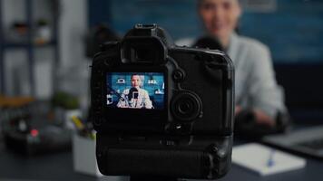 Professional camera recording social media influencer daily vlog while talking to audience. Digital content creator having modern equipment filming while sitting at studio desk. Close up video