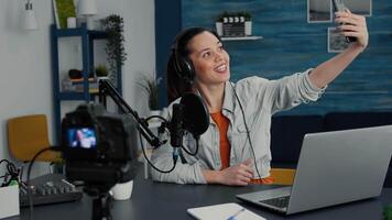 Famous internet influencer taking selfie photo with smartphone while streaming. Creative content creator sitting in home studio while taking pictures with touchscreen mobile phone. video