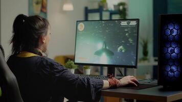 Woman gamer with headset looking at camera smiling and playing virtual shooter game championship in cyberspace, esports player performing on powerful computer in stylish room during gaming tournament video
