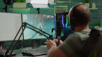 Entusiastic man gamer streamer wining space shooter games holding joystick playing on professional RGB keyboard and talking on stream chat. Pro cyber using microphone in gaming tournament video