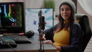 Woman looking at camera sitting in front of RGB powerful computer playing online space shooter videogame streaming game on internet. Pro cyber videogamer playing games in gaming home studio video