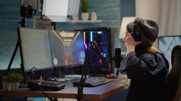 Streamer putting on headphone and start talking into microphone with other players during online game professional competition. Pro gamer sitting on gaming chair in streaming home studio with RGB video