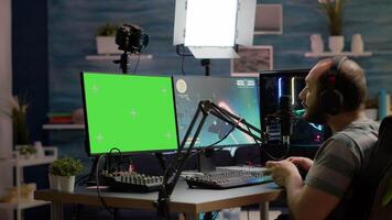 Gamer streaming online videogames on professional powerful computer with green screen, mock up, chroma key display. Streamer playing space shooter game at isolated desktop holding wireles controller video