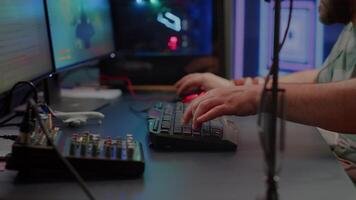 Close up of streamer typing at RGB keyboard playing space shooter videogame. Pro cyber man using mixer sound in gaming home studio for online esports competition on professional powerful computer video