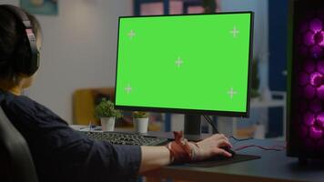 Woman gamer streaming online games on powerful computer with green screen mock up, chroma key display. Cyber player using professional pc with isolated desktop streaming shooter games in headset video