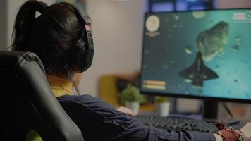 Focused woman gamer sitting on desk, putting on headset with a mic and starts playing space shooter game. Online streaming cyber performing on powerful personal computer during gaming tournament video