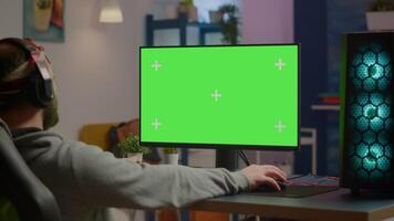 Pro gamer streaming games with green screen mock-up display in gaming home studio. Player using RGB professional computer with chroma key isolated desktop playing shooter games wearing headset video