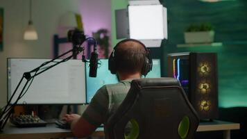 Back shot of streamer man playing on powerful computer shooter game for tournament, talking with multiple players into headphones. Pro gamer using professional streaming equipment video