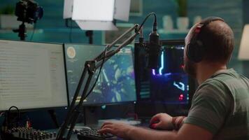 Over shoulder footage of professional streamer with headset playing digital space shooter games on RGB powerful computer using microphone and mouse. Videogamer man streaming online games video