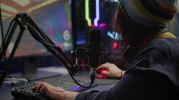 Close-up of streamer playing first person shooter game using RGB keyboard and mouse. Gamer talking on streaming chat with other players during esport tournament late at night in gaming studio video