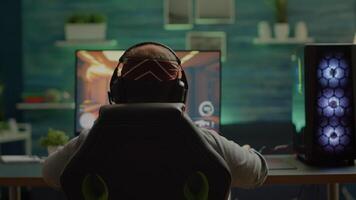 Back shot of happy gamer winning first person shooter game playing online on RGB powerful personal computer raising hands. Pro cyber performing during virtual tournament using technology network video