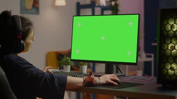 Pro woman player gaming on powerful computer with green mock up chroma key screen while streaming online competition. Gamer using pc with greenscreen isolated desktop streaming shooter games video