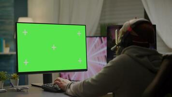 Professional cyber gamer playing games with greenscreen, chroma key, mock up desktop isolated display. Player using powerful computer with mockup screen streaming shooter games wearing headset video
