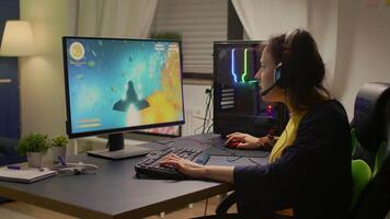 Gamer playing online space shooter games using powerful computer and RGB keyboard. Player wearing headphones and talking into microphone with other players for winning online tournament video