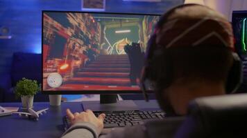 Back shot of pro esport gamer playing first person shooter game on powerful computer using RGB keyboard. Competitive player man streaming online game for tournament using professional equipment video