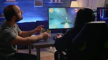 Couple of gamers losing space shooter tournament while playing in room with RGB. Defeated player with headphones streaming online cyber performing during online gaming competition. video
