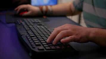 Close-up of streamer man playing space shooter game using RGB keyboard during esport tournament. Player performing online competition late at night in streaming home studio video
