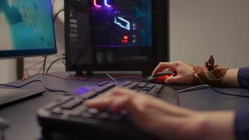 Close-up of gamer using RGB keyboard and mouse for online competition. Professional gamer playing space shooter games in gamming room with neon light video