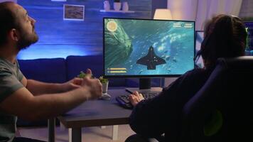 Couple of gamers making winner gesture while playing space shooter virtual championship. Defeated player with headphones streaming online cyber performing during online gaming competition. video