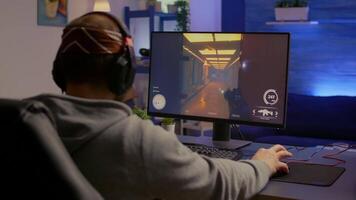 Back of pro gamer playing first person shooter game on professional computer for cyber esport competition. Pro player talking with multiple players using headset during online tournament video