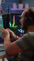 Vertical . Concentrated gamer playing shooter game in gaming competition using wireless controller wearing professional headphones. Online streaming cyber performing during tournament using RGB powerful PC video