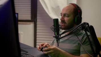Close-up of pro streamer talking into professional microphone during virtual competition. Player streaming online games using wireless controller late at night in gaming home studio video