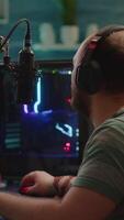 Vertical . Over shoulder footage of professional streamer with headset playing digital space shooter games on RGB powerful computer using microphone and mouse. Videogamer man streaming online games video