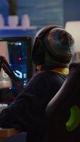 Vertical . Focused streamer playing shooter game for virtual competition using professional headphones. Online streaming cyber performing during gaming tournament using powerful PC with RGB and stream open chat video